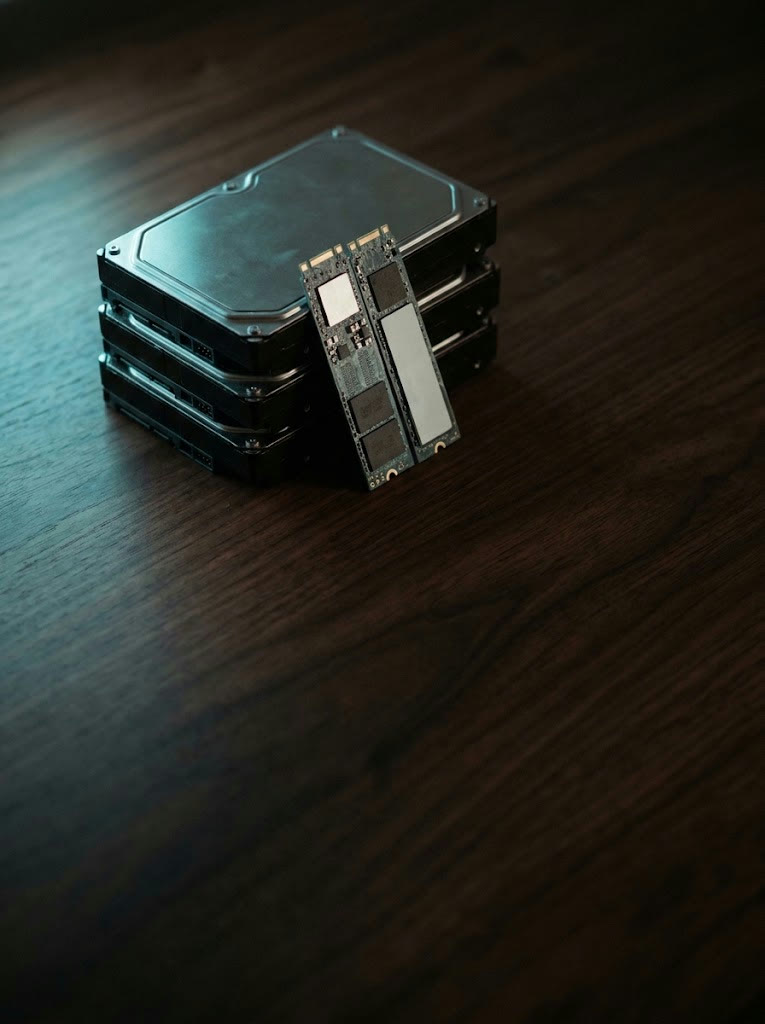 Three hard drives stacked on a dark wooden desk with two NVMe SSDs leaning against them