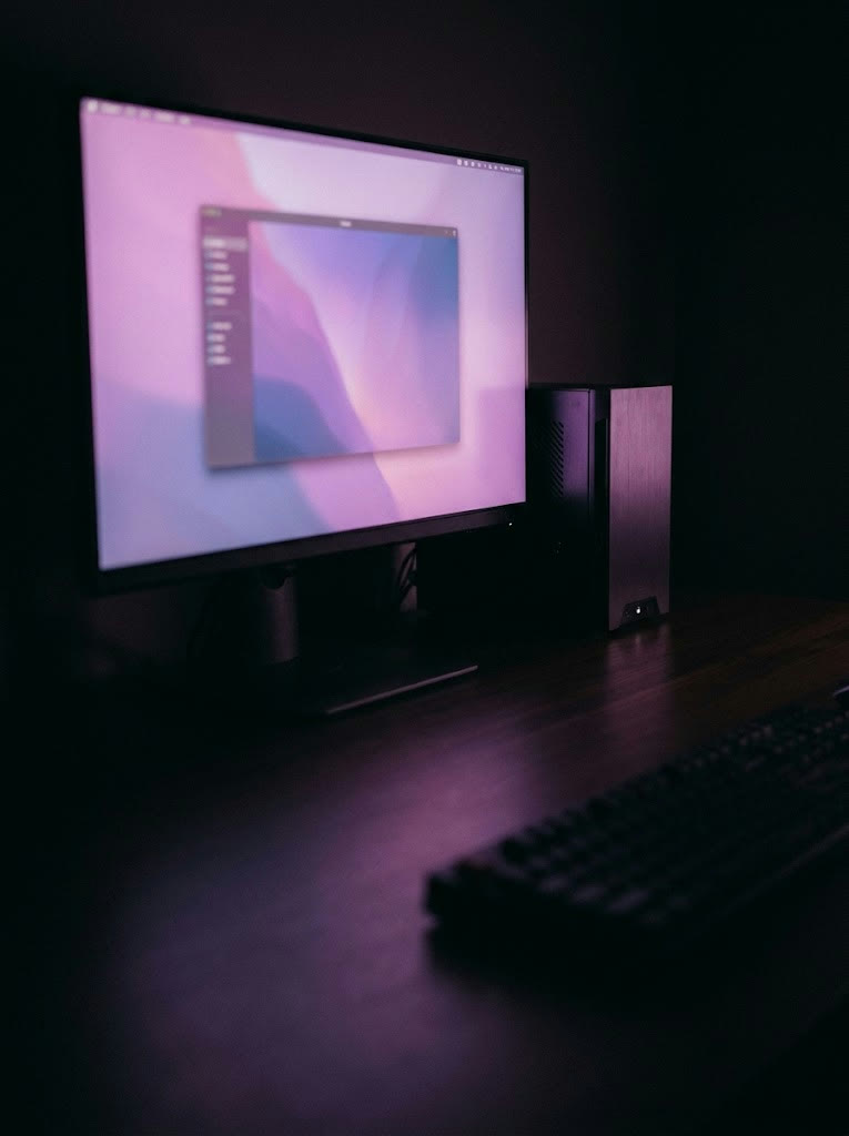 A desk at night with a monitor showing a second desktop in a window, a small server beside it